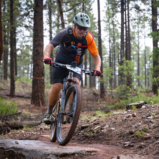 Peter racing a mountain bike through a pine forest on a wet trail